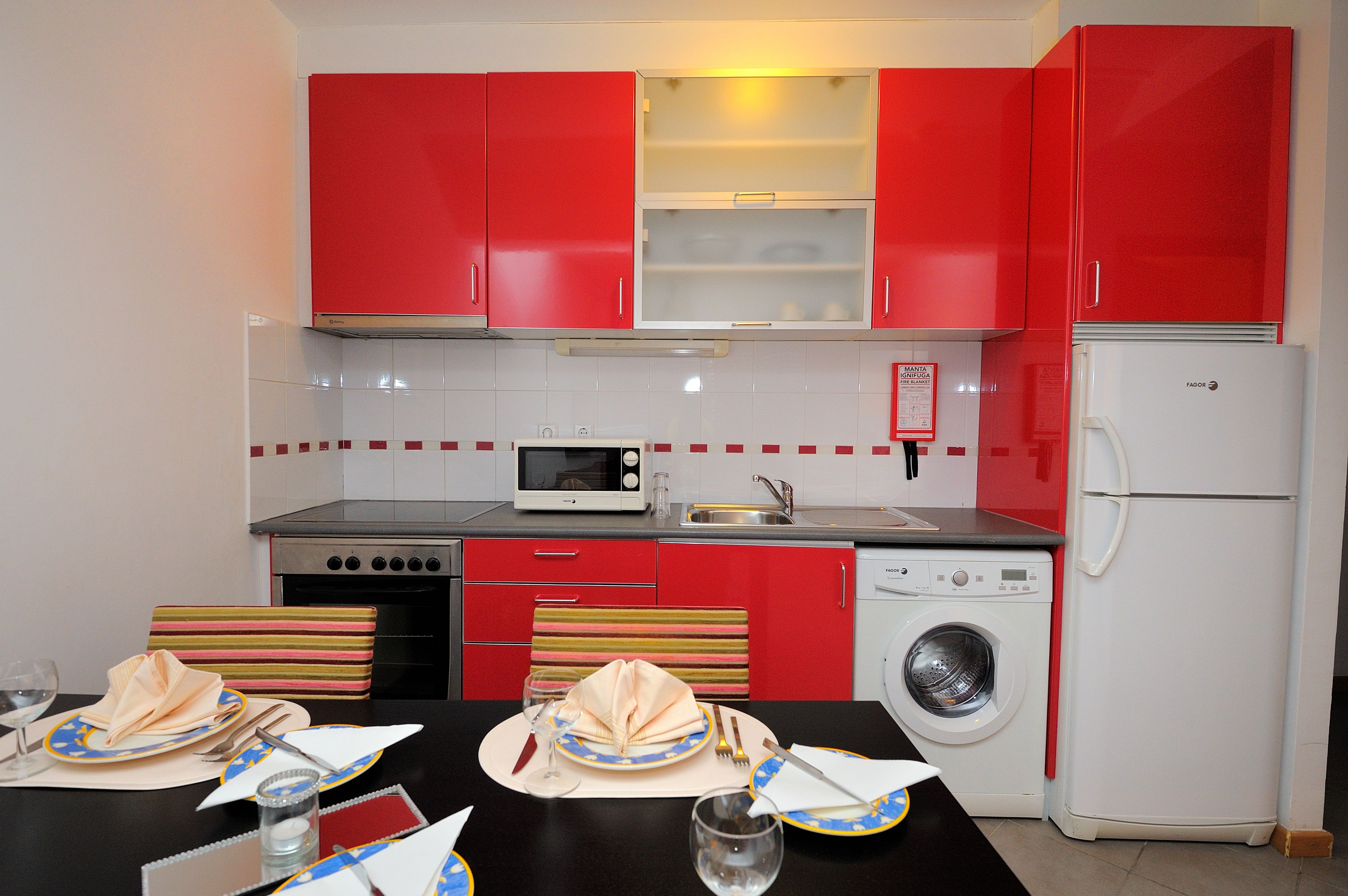 Una cocina compacta con armarios rojos, microondas, estufa, lavaplatos y lavadora.