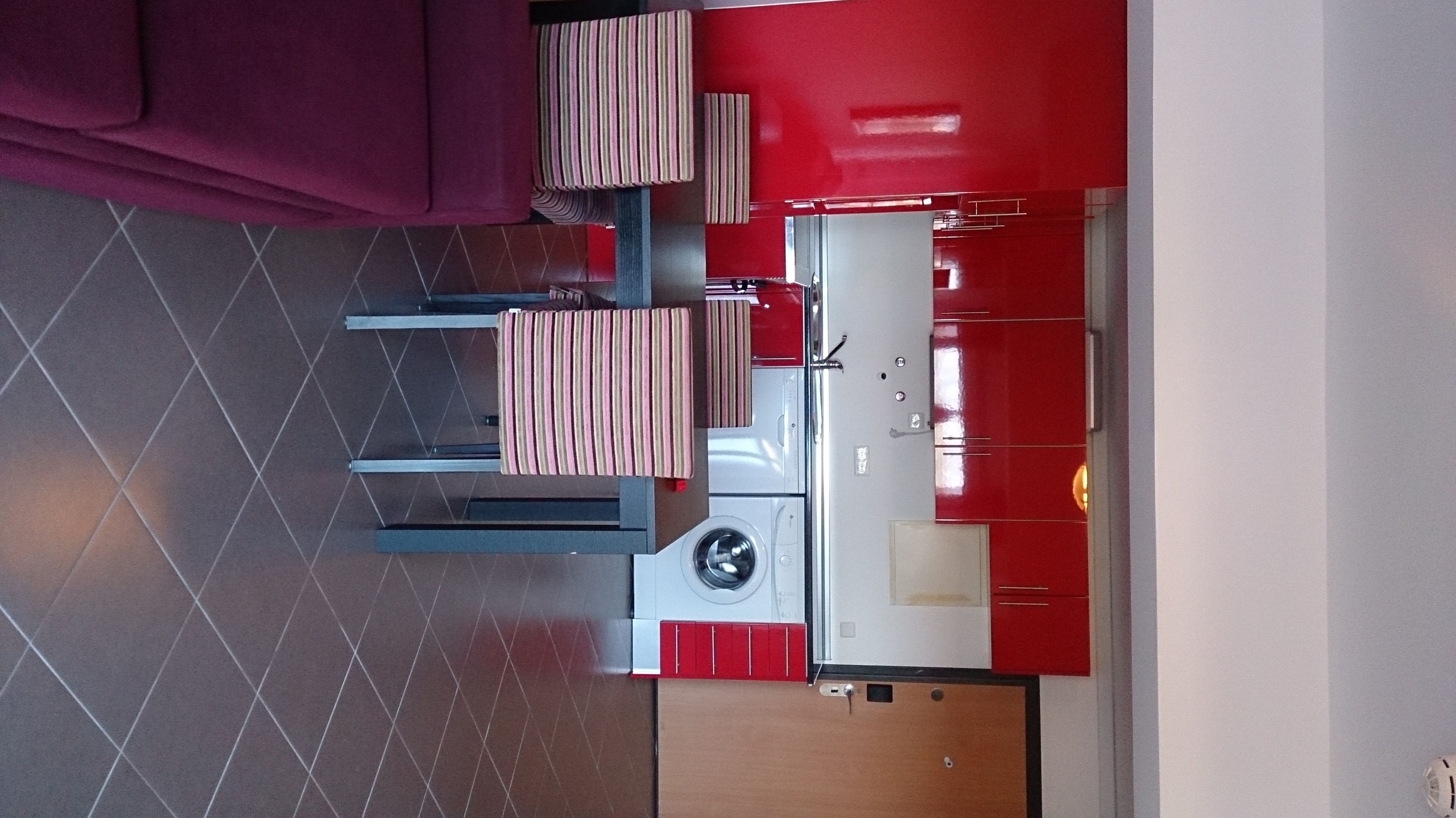 A compact kitchen with a red and white color scheme, a washing machine, and a dining area with striped cushions.