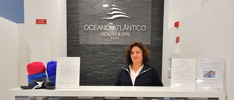 A reception desk with a logo for Ocean Atlantico Health & Spa, a white counter, and a patterned wall.
