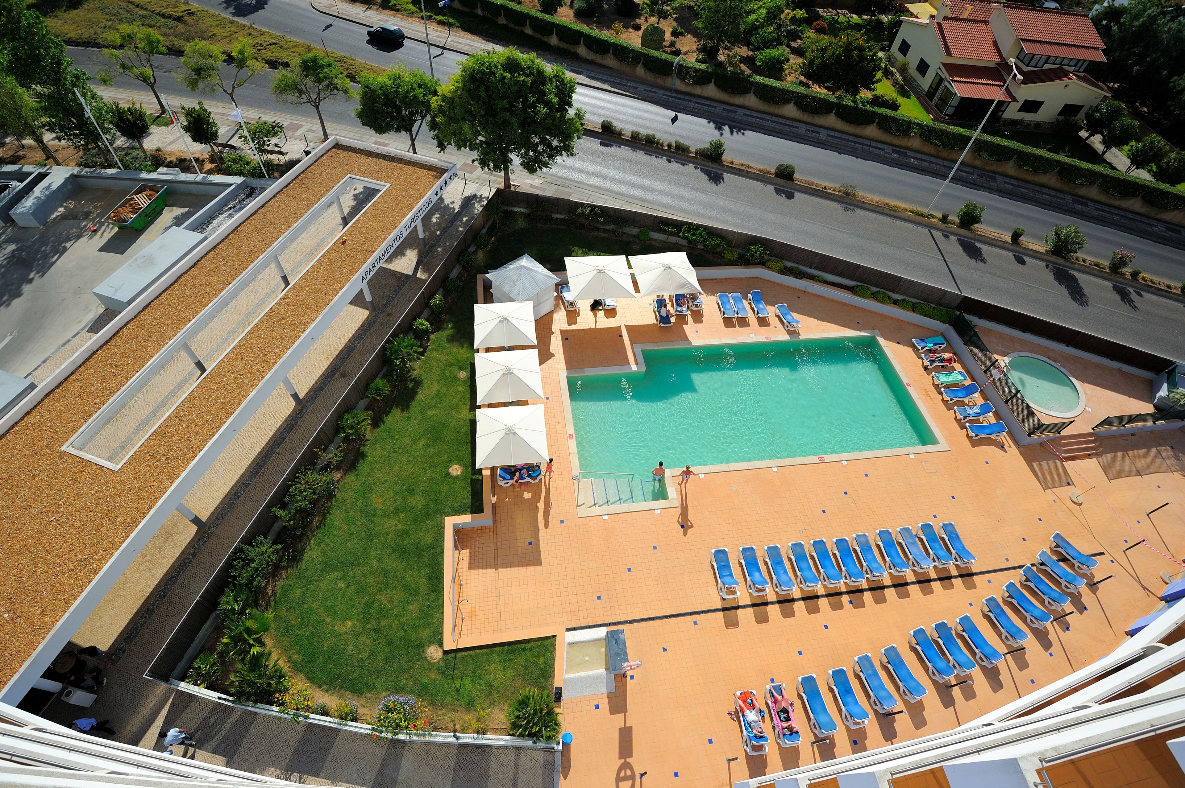 An aerial view of a hotel with a swimming pool, sun loungers, and a small boat.