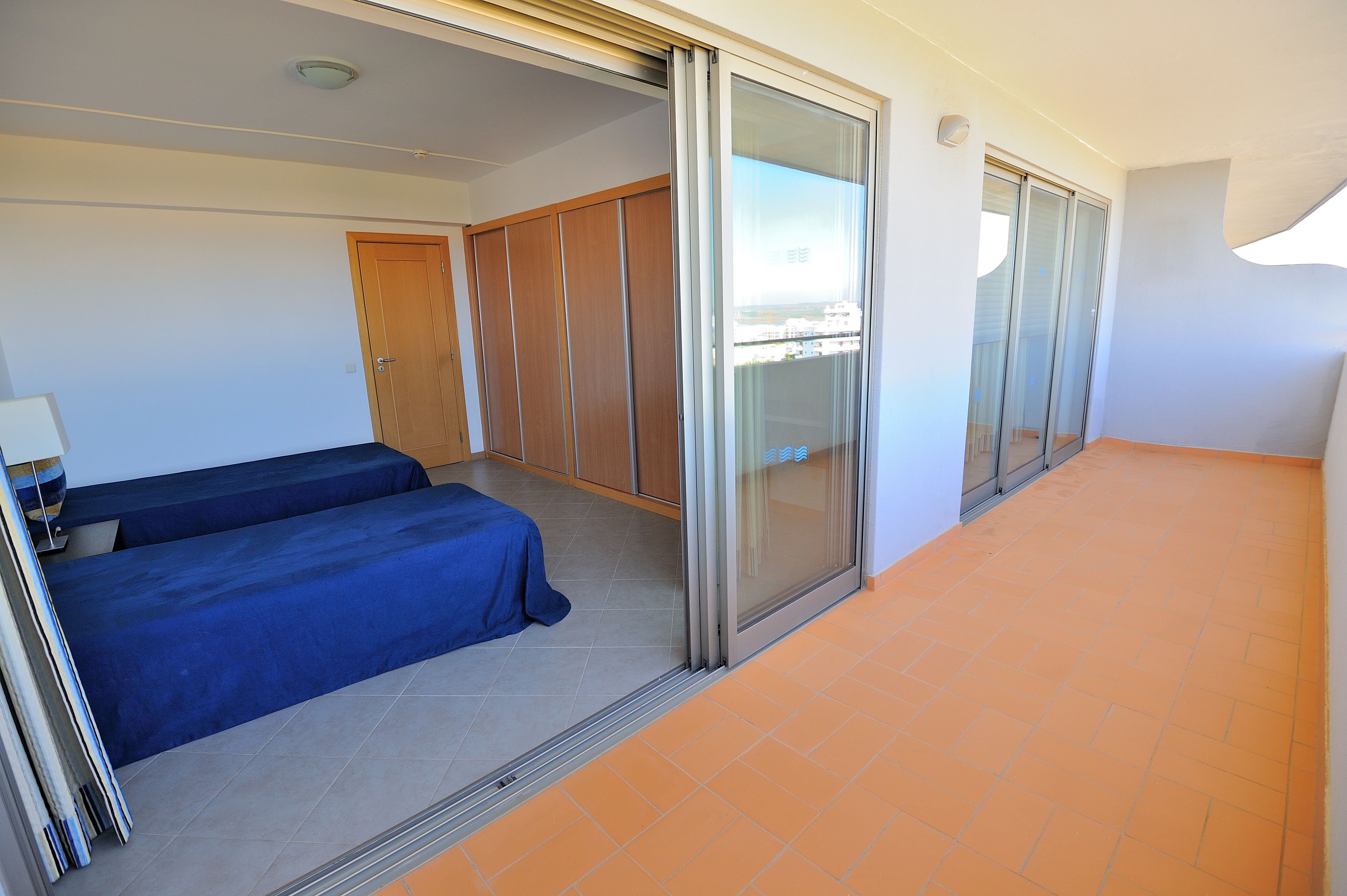 A hotel room with a bed, a wardrobe, a sliding glass door, and a tiled floor.