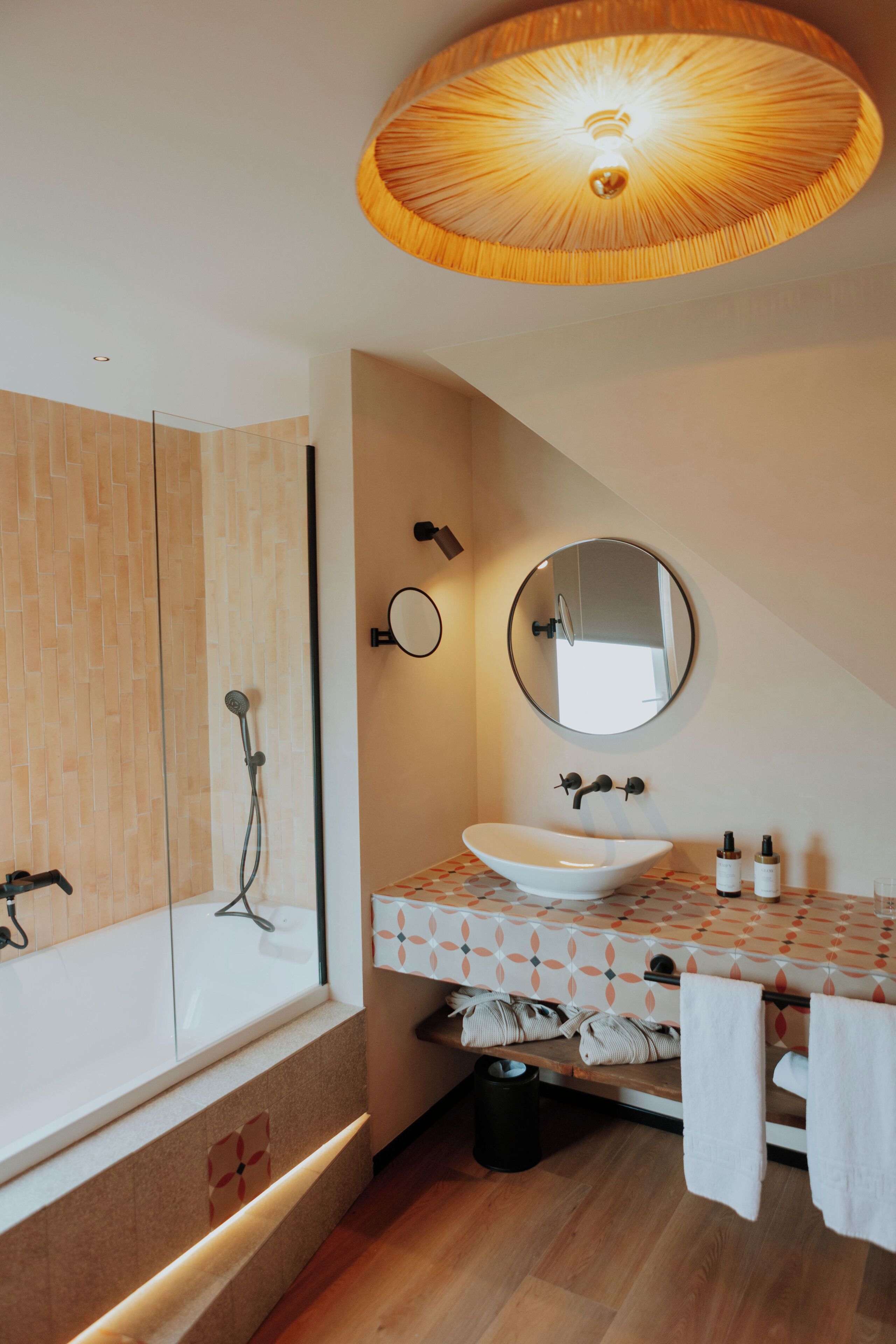 A modern bathroom with a bathtub, a round mirror, a sink, and a ceiling light fixture.