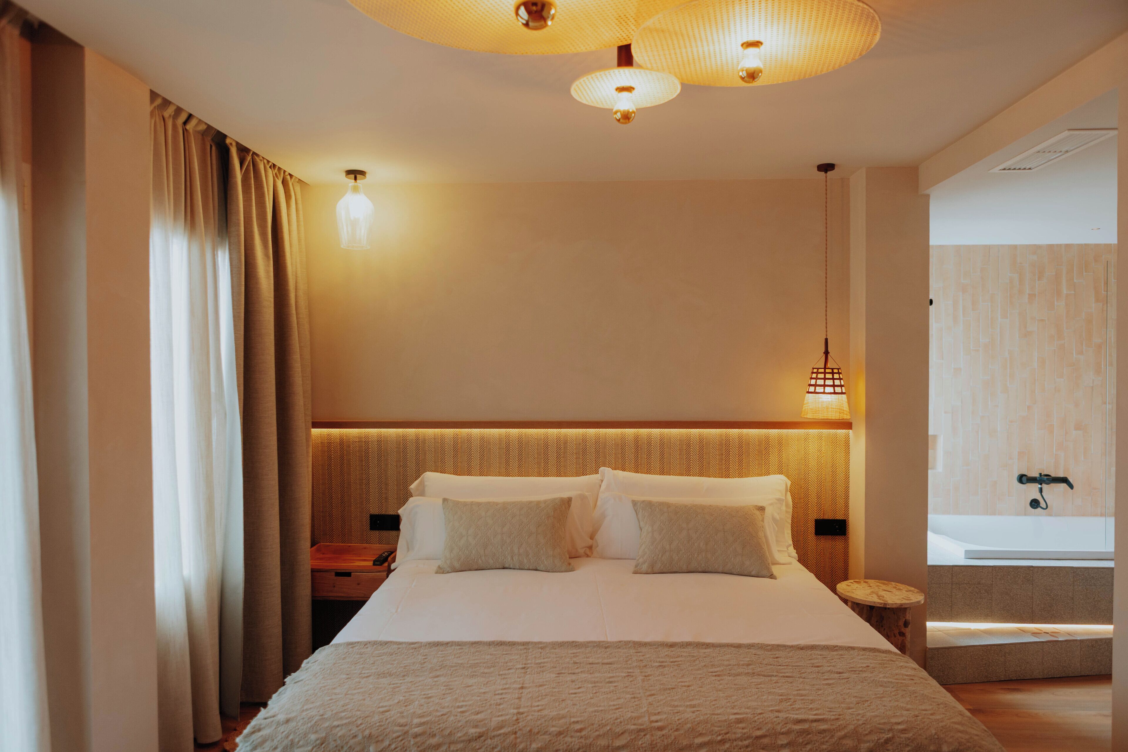 Habitación de hotel con una cama grande, mesitas de noche, lámpara de pared y vistas al baño.