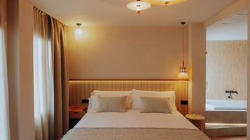 A hotel room with a large bed, bedside tables, a nightstand, a wall-mounted lamp, and a view of a bathroom.