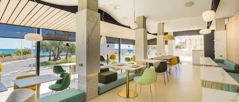 Un restaurante moderno con vista al mar, que ofrece una variedad de opciones de asientos, incluyendo mesas y bancos, y una diversidad de sillas coloridas.