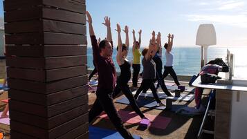 Un grupo de personas practicando yoga en esterillas frente a una ventana con vista al océano.