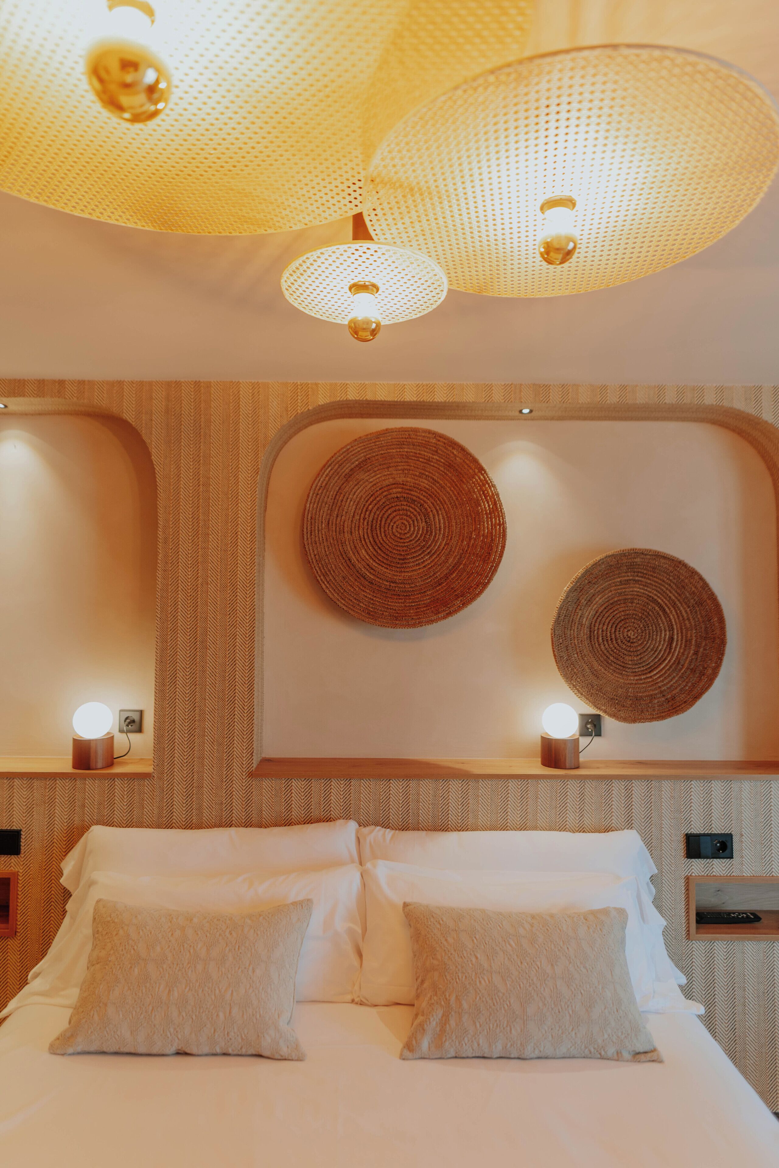 Una habitación de hotel con una cama, dos lámparas de pared y dos adornos tejidos para la pared.