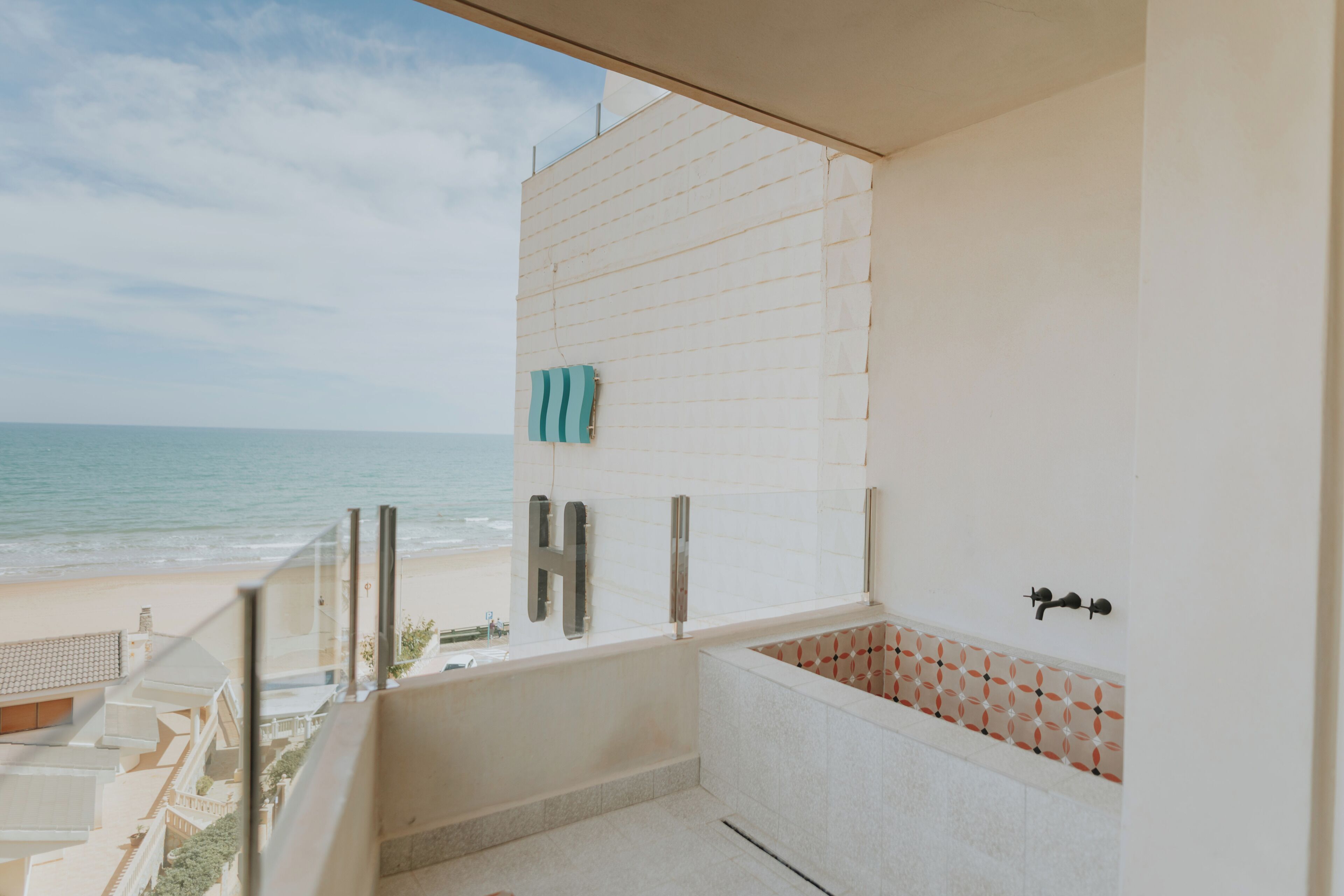 Un balcón con vista a la playa y al océano, una bañera y una toalla colgada en la pared.