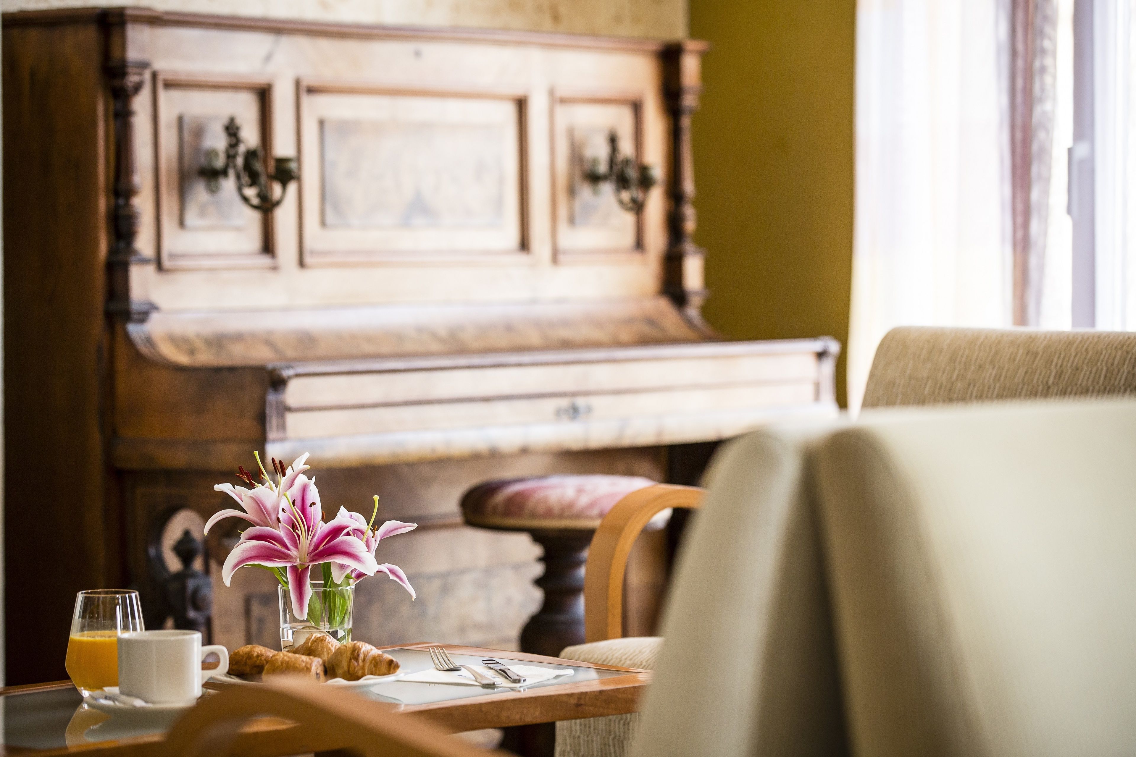 A breakfast setup with croissants, a coffee cup, and a vase of flowers on a table.