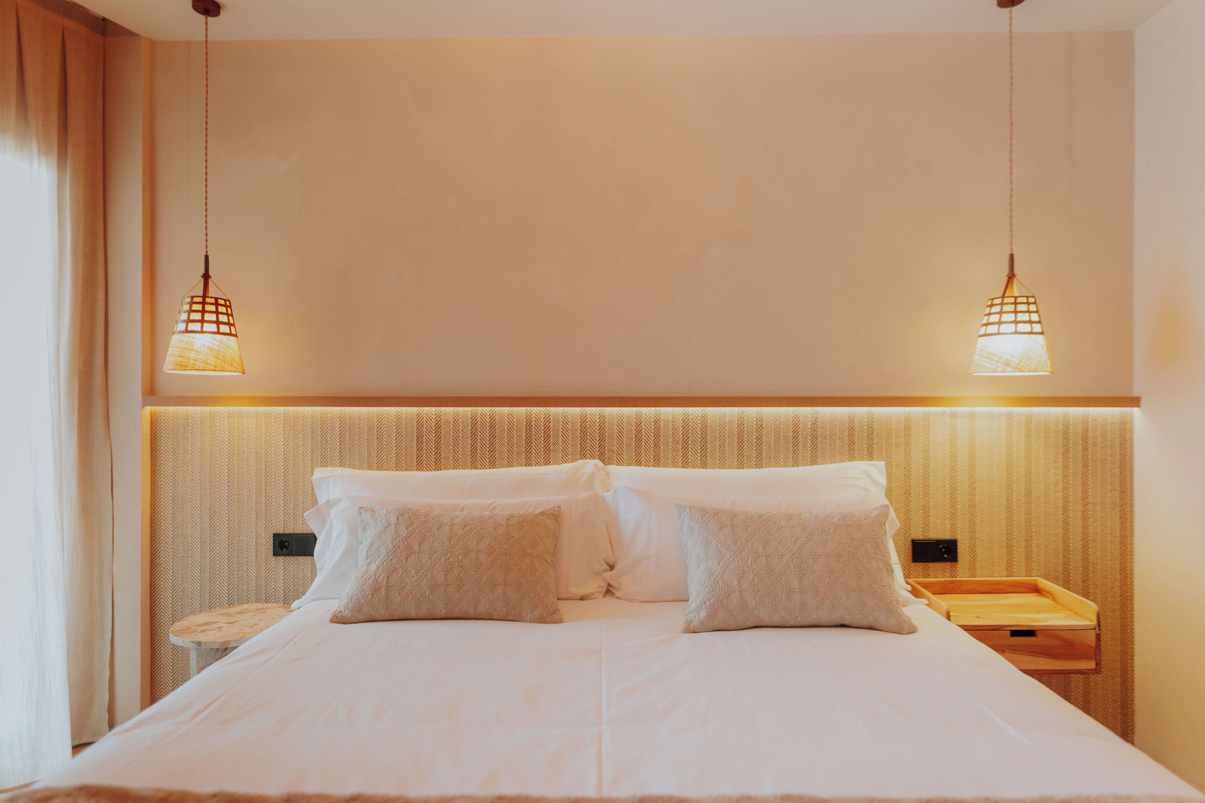 A neatly made bed with white linens and two pillows, a bedside table with a lamp, and a headboard with a textured pattern.