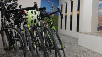 Bicicletas estacionadas en el interior junto con cascos y un esquílero de pared.