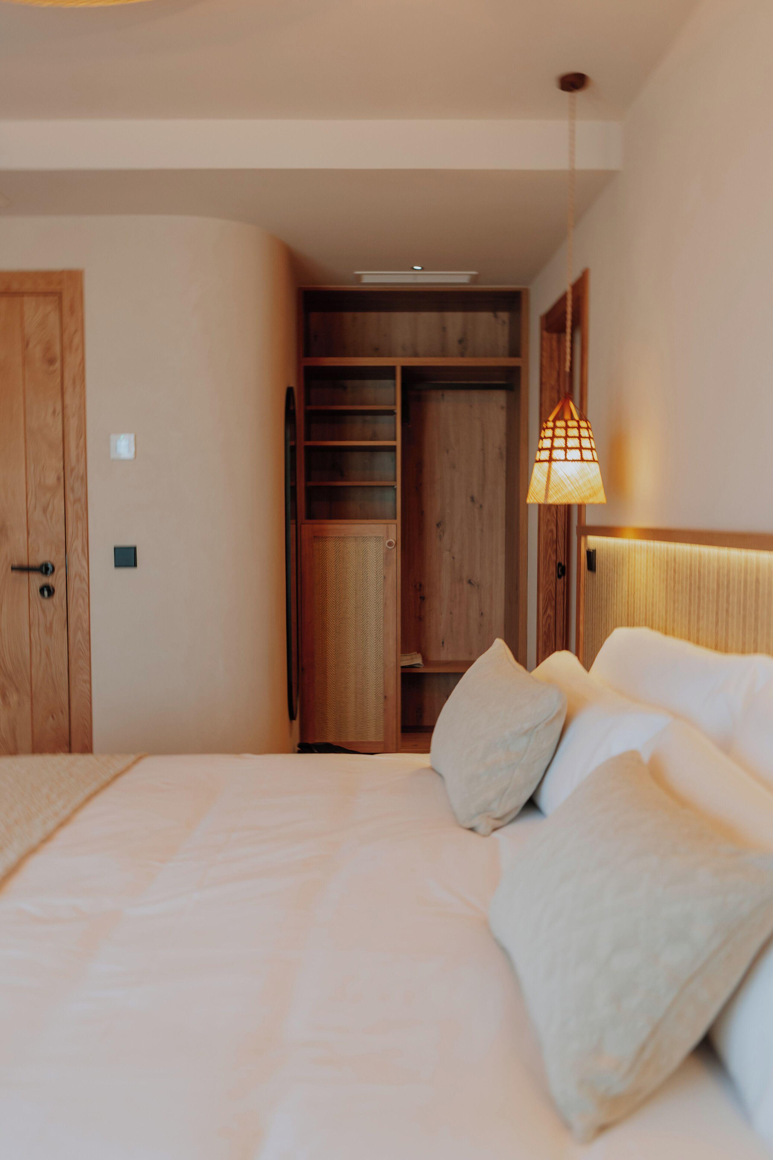 Un dormitorio con cama, armario de madera y lámpara colgante.