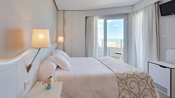 Una habitación de hotel con cama, escritorio, televisor y vista al mar.
