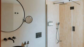 A modern bathroom with a round mirror, a black basin, a toilet, and a glass-enclosed shower.