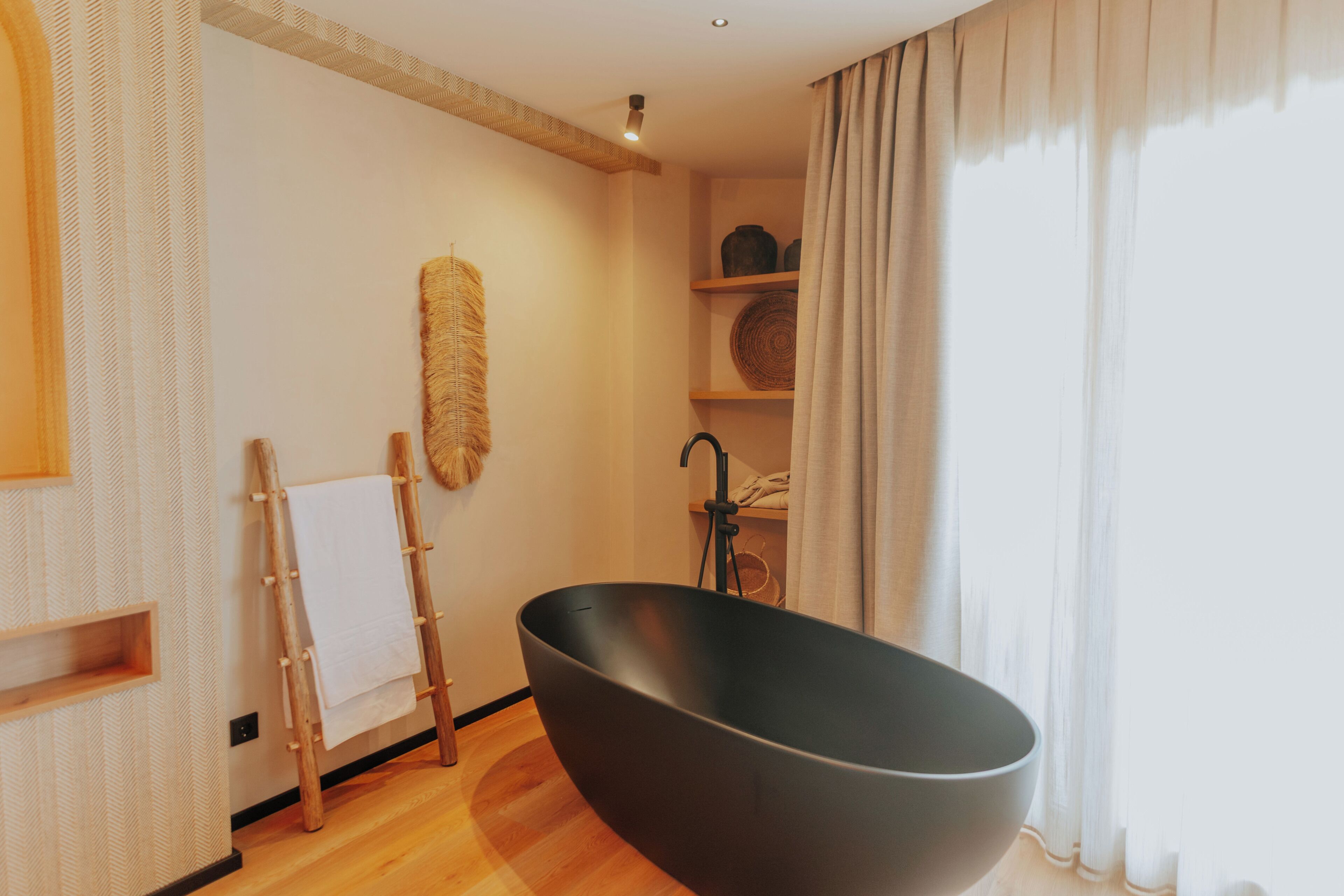 Un baño moderno con una bañera independiente, suelo de madera y un estante con toallas.