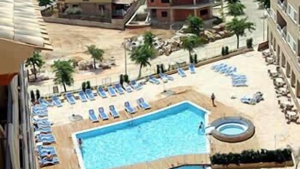 A resort with a swimming pool, lounge chairs, and a view of the sea.