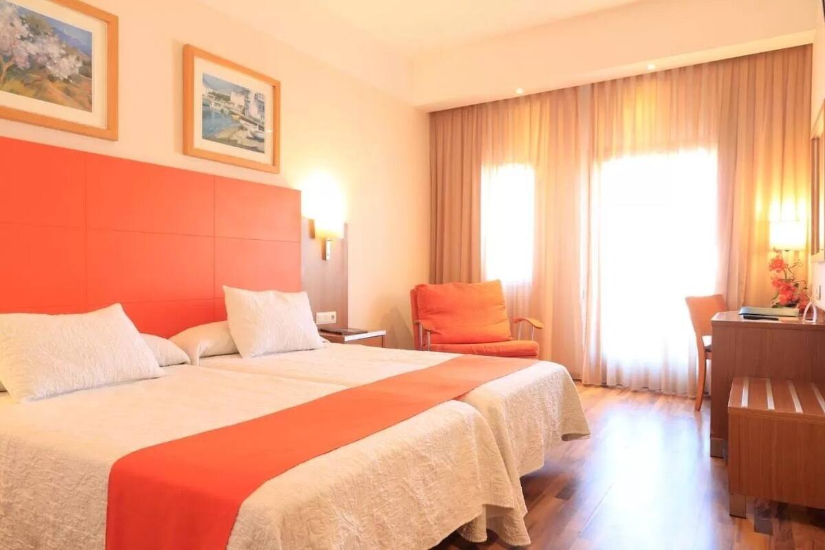 Une chambre d’hôtel avec un grand lit, un bureau et une chaise. Deux tableaux encadrés sont accrochés au mur.