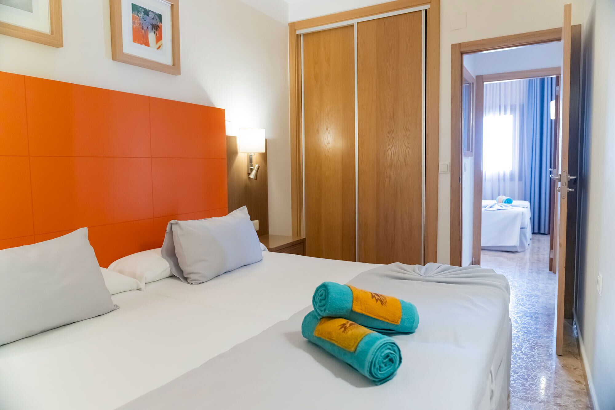 Een hotelkamer met een bed, een kledingkast, een nachtkastje en uitzicht op een andere kamer.