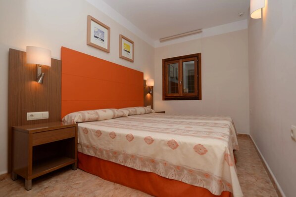 Un dormitorio con cama, mesita de noche, lámparas de pared y cuadros enmarcados.