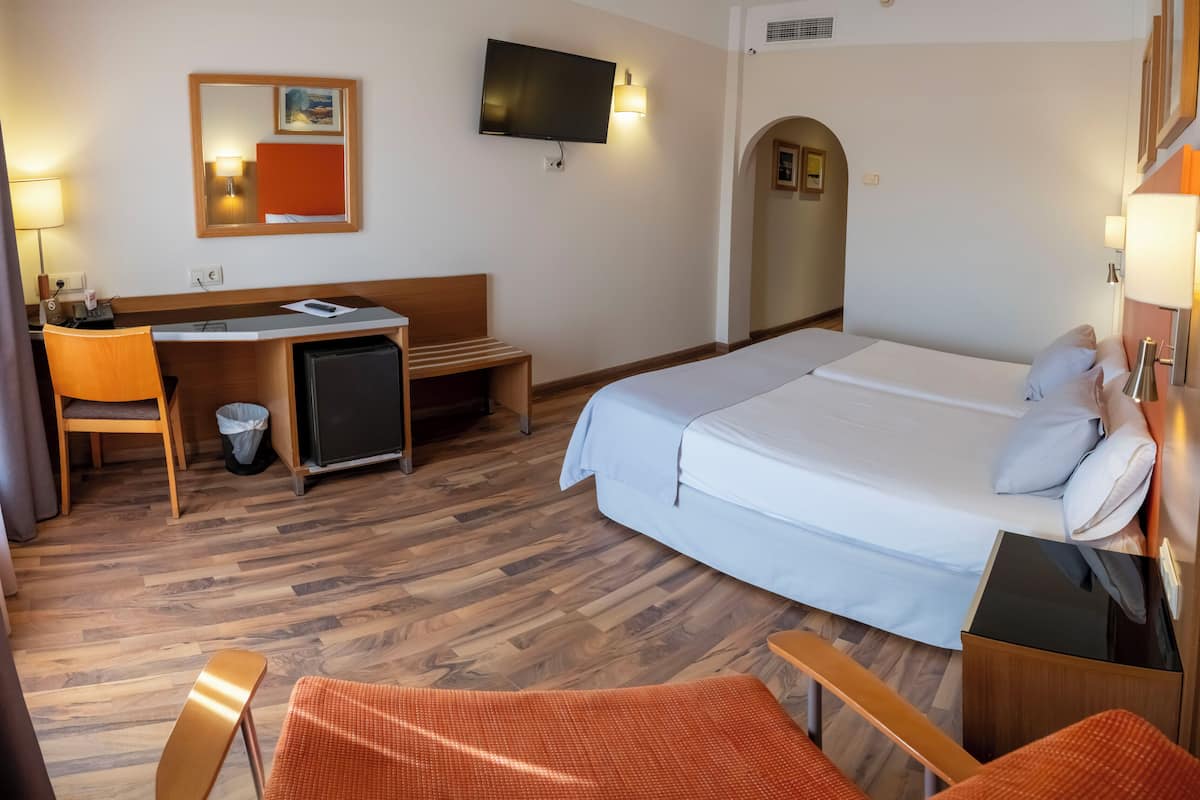A hotel room with a bed, desk, chair, and TV.