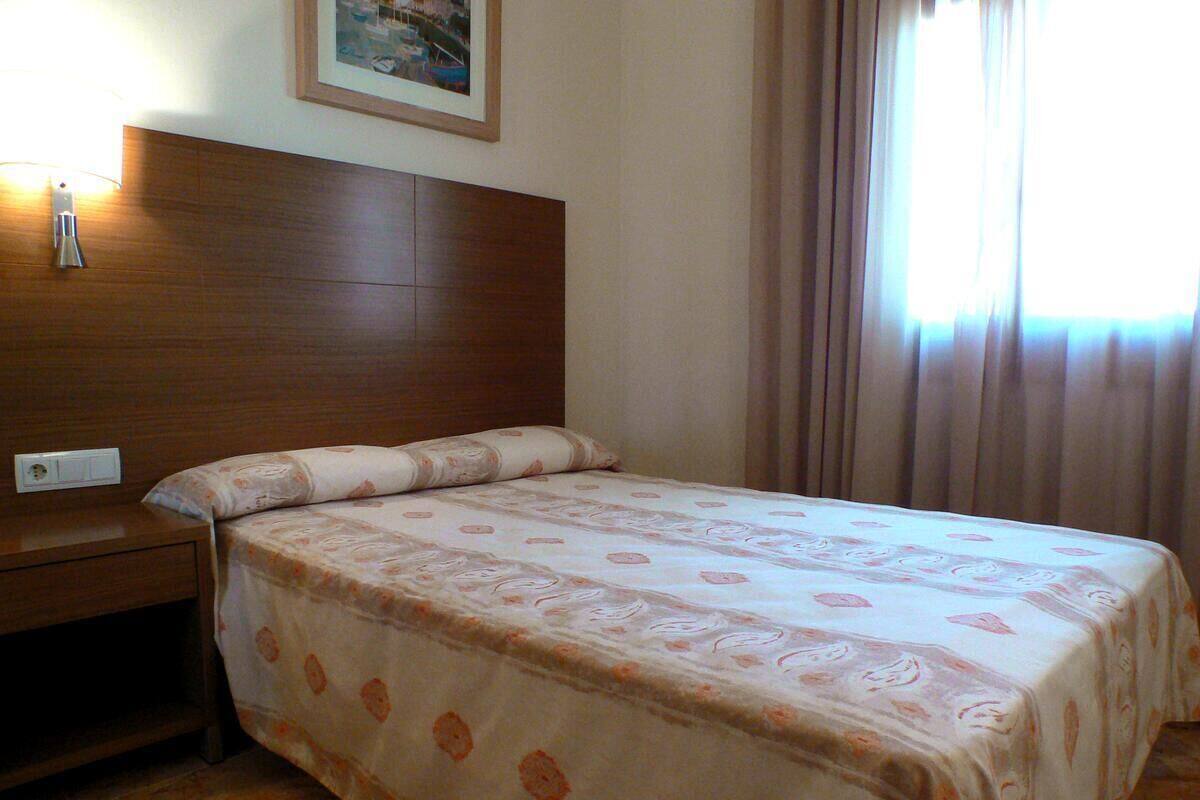 Une chambre d’hôtel avec une tête de lit en bois, un lit recouvert d’une couvre-lit à motifs floraux, une table de chevet et une lampe fixée au mur.