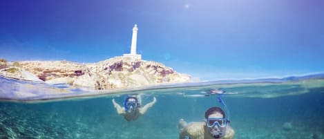 Two people snorkeling near a rocky island with a lighthouse.