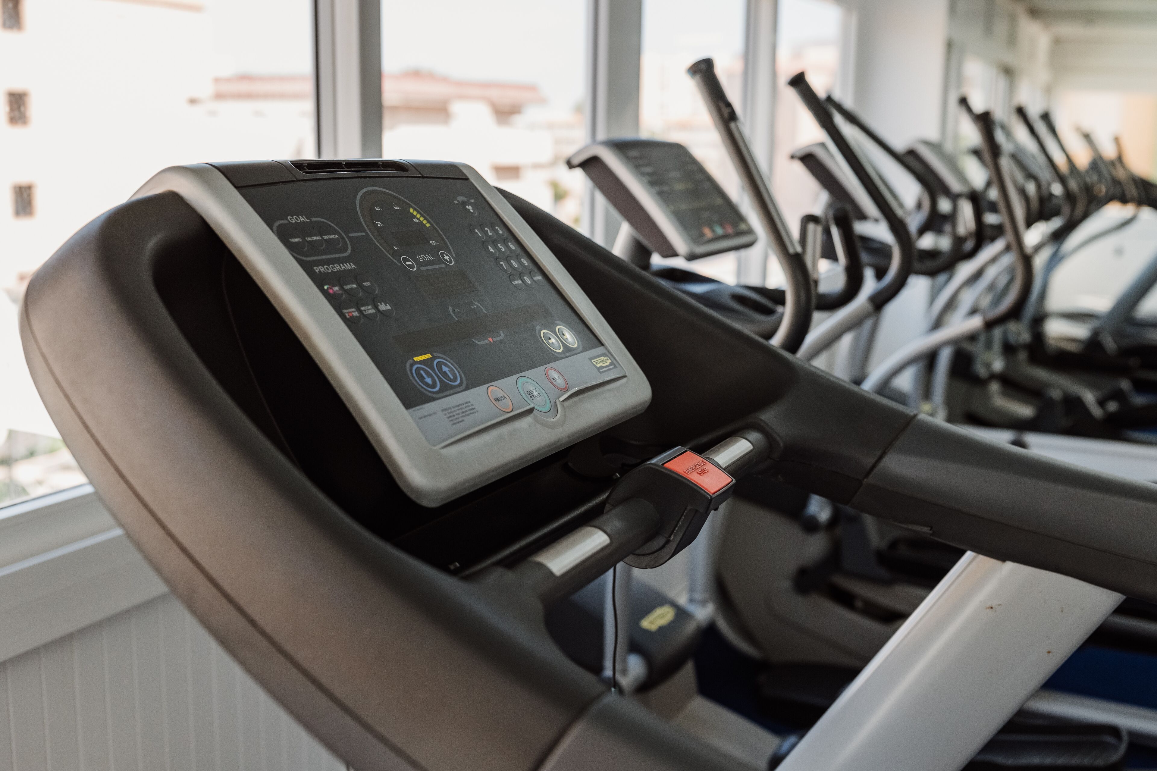 A treadmill with a digital display and a control panel, located in a gym with multiple treadmills in the background.
