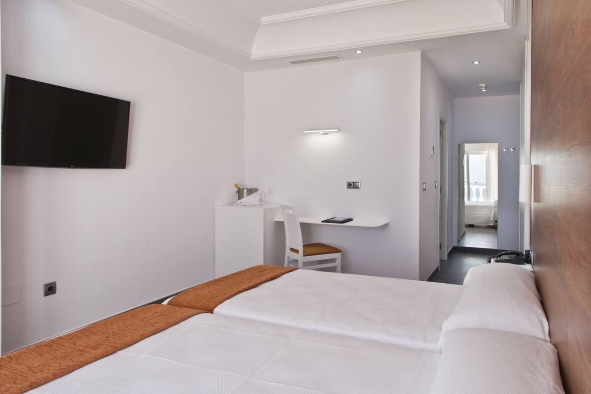 A hotel room with a large bed, a desk with a chair, a television mounted on the wall, and a bathroom visible through an open door.