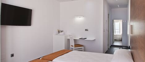 A hotel room with a large bed, a desk with a chair, a television mounted on the wall, and a bathroom visible through an open door.