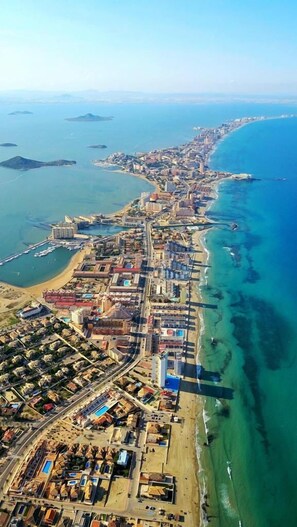Vista aérea de una ciudad costera con una zona urbana densa, un puerto deportivo y una playa.