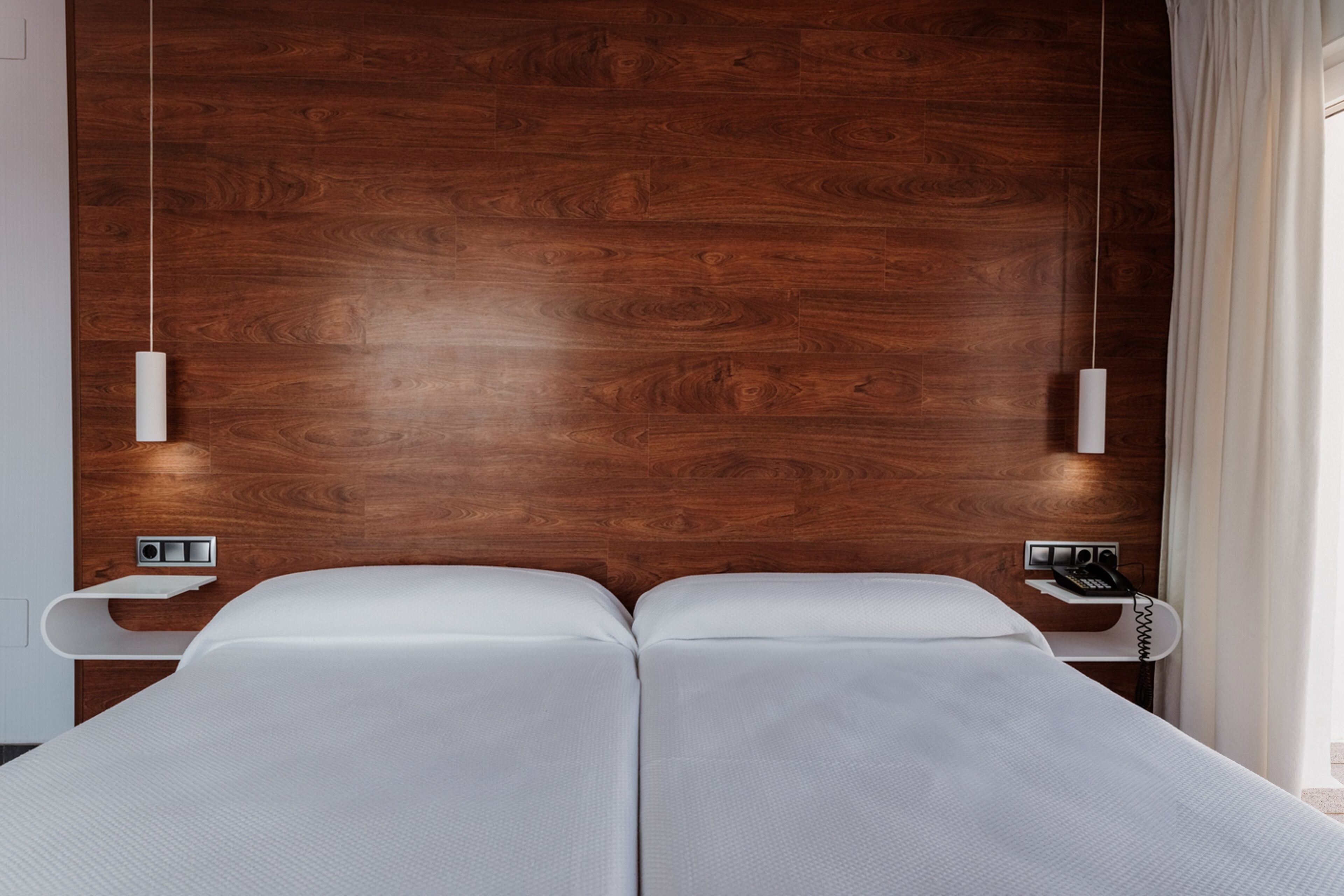 A modern hotel room with a wooden headboard, two beds, bedside tables, and a telephone.