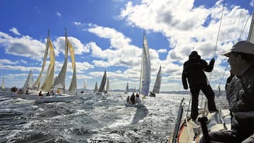 Un velero con varias velas, personas a bordo y un cielo despejado con nubes.