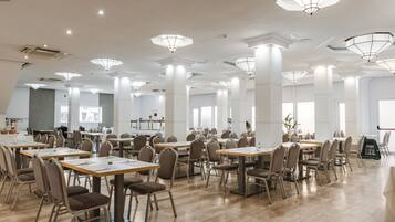 A spacious conference room with multiple tables and chairs, large windows, and modern ceiling lights.