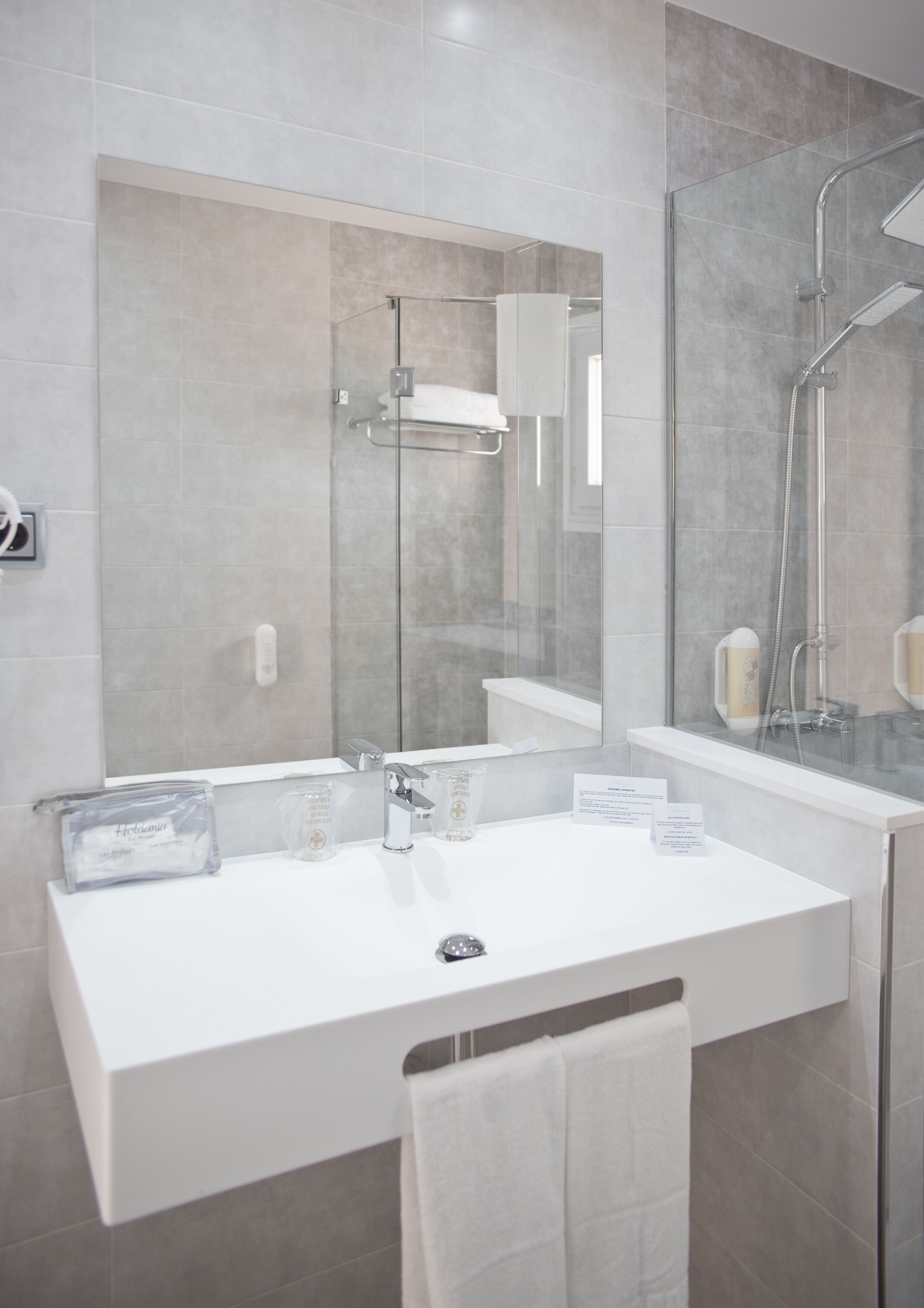 A modern bathroom with a white sink, mirror, and glass-enclosed shower.