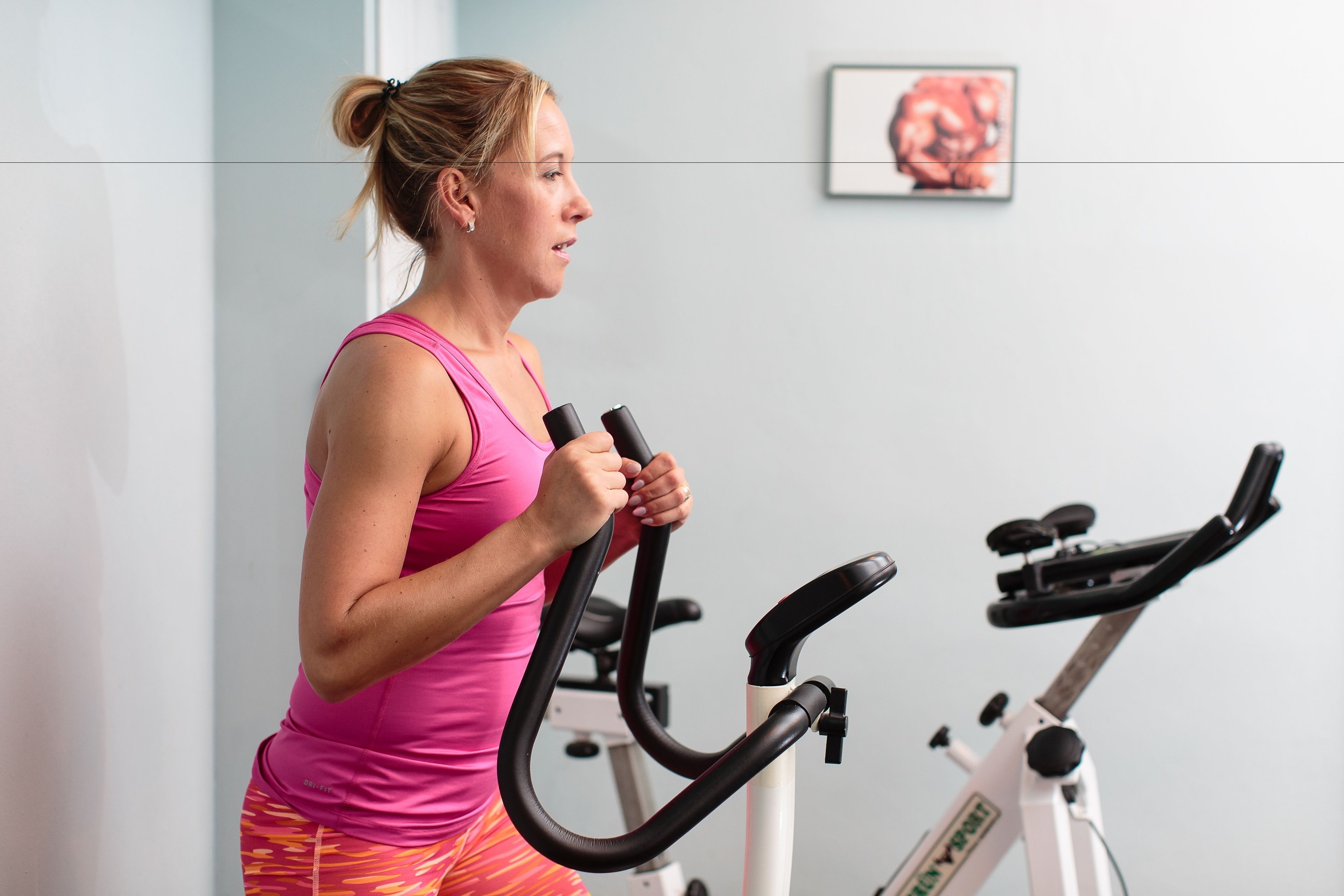 Una persona usando una bicicleta estática en una habitación con una pared lisa y un cuadro enmarcado.