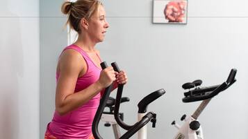Una persona usando una bicicleta estática en una habitación con una pared lisa y un cuadro enmarcado.