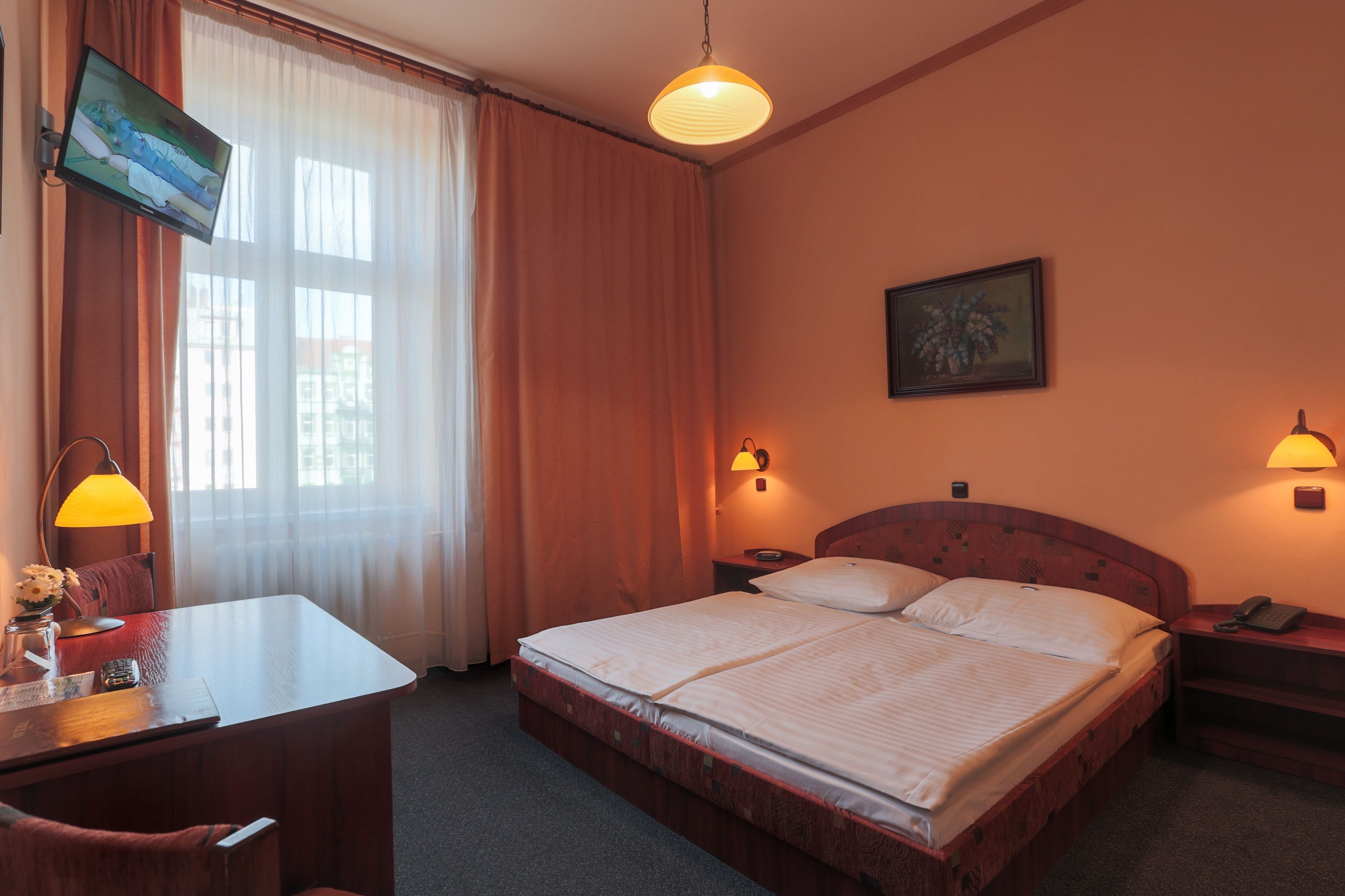 A hotel room with a bed, a desk, a television, and two bedside lamps.