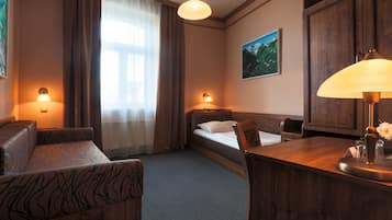 Una habitación de hotel con una cama, dos mesitas de noche con lámparas, un escritorio de madera, una silla, un sofá y un ventanal con cortinas.