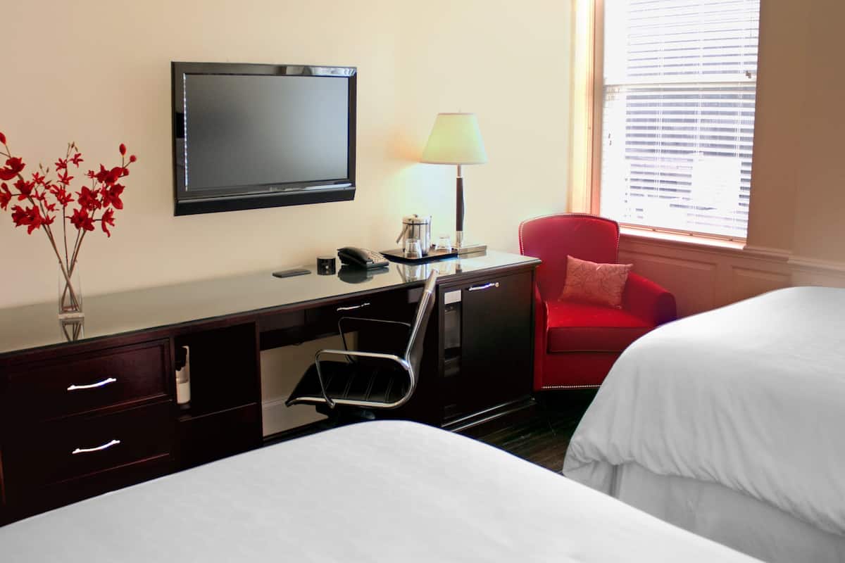 A hotel room with a bed, a desk with a chair, a television, a lamp, and a window with blinds.