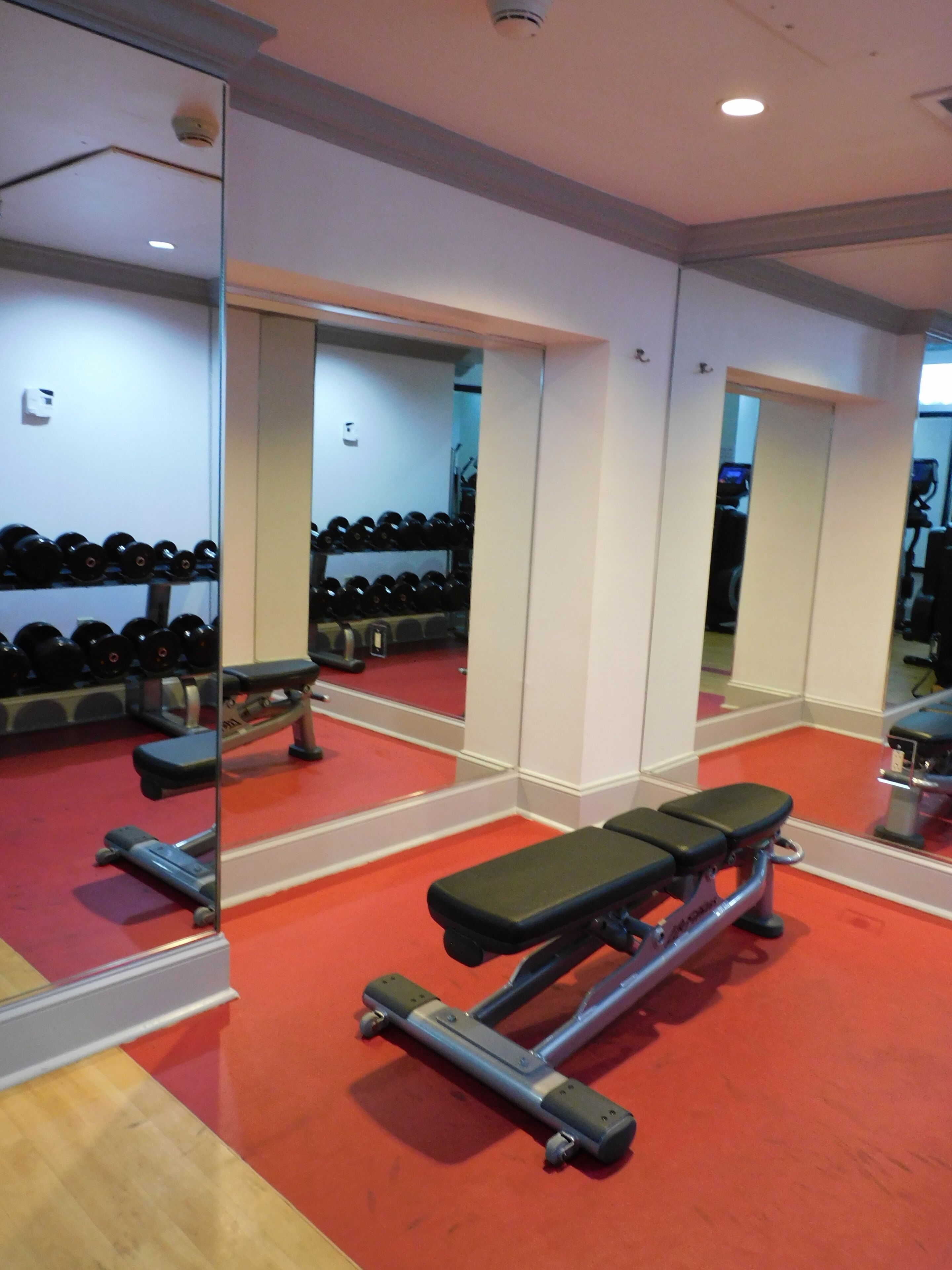 A gym with mirrored walls, red flooring, and weightlifting equipment.