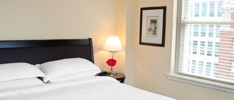 A neatly made bed with white linens, a bedside lamp, and a framed picture on the wall.