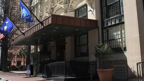 A historic building with ornate architectural details, a prominent entrance, and flags.