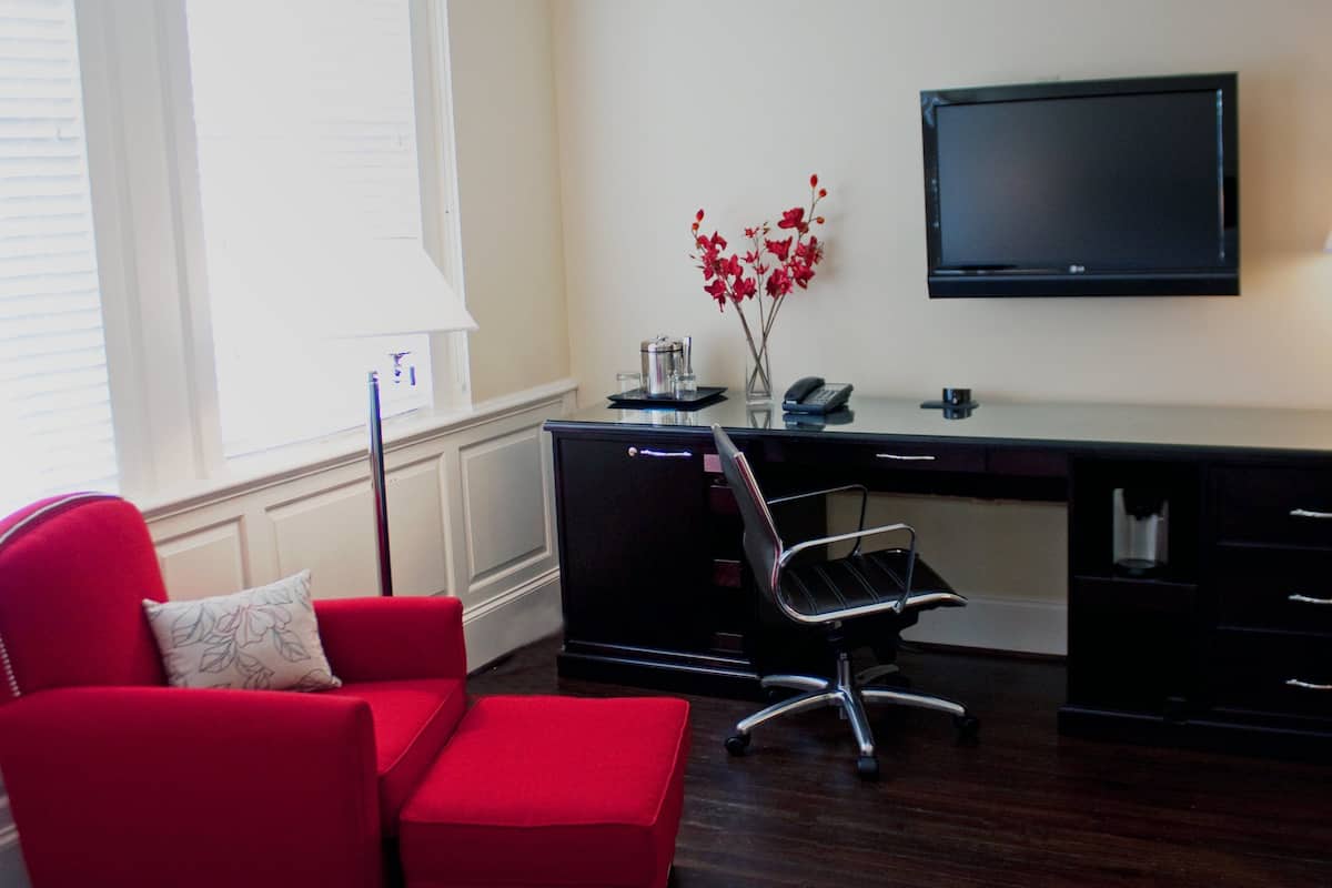 A modern office space with a desk, chair, TV, and a red sofa.