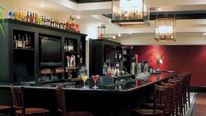 A bar area with a long counter, multiple bar stools, and a variety of bottles and glasses.