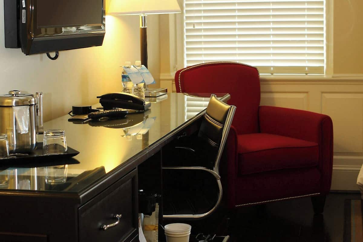 A hotel room with a desk, a chair, a television, a lamp, a coffee maker, and a window with blinds.