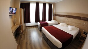 A hotel room with two beds, a desk, a TV, and a window with curtains. - Hotel de France (Brussels)