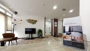 A modern hotel lobby with a marble floor, a flat-screen TV, a plant, and a poster for Hotel de France. - Hotel de France (Brussels)