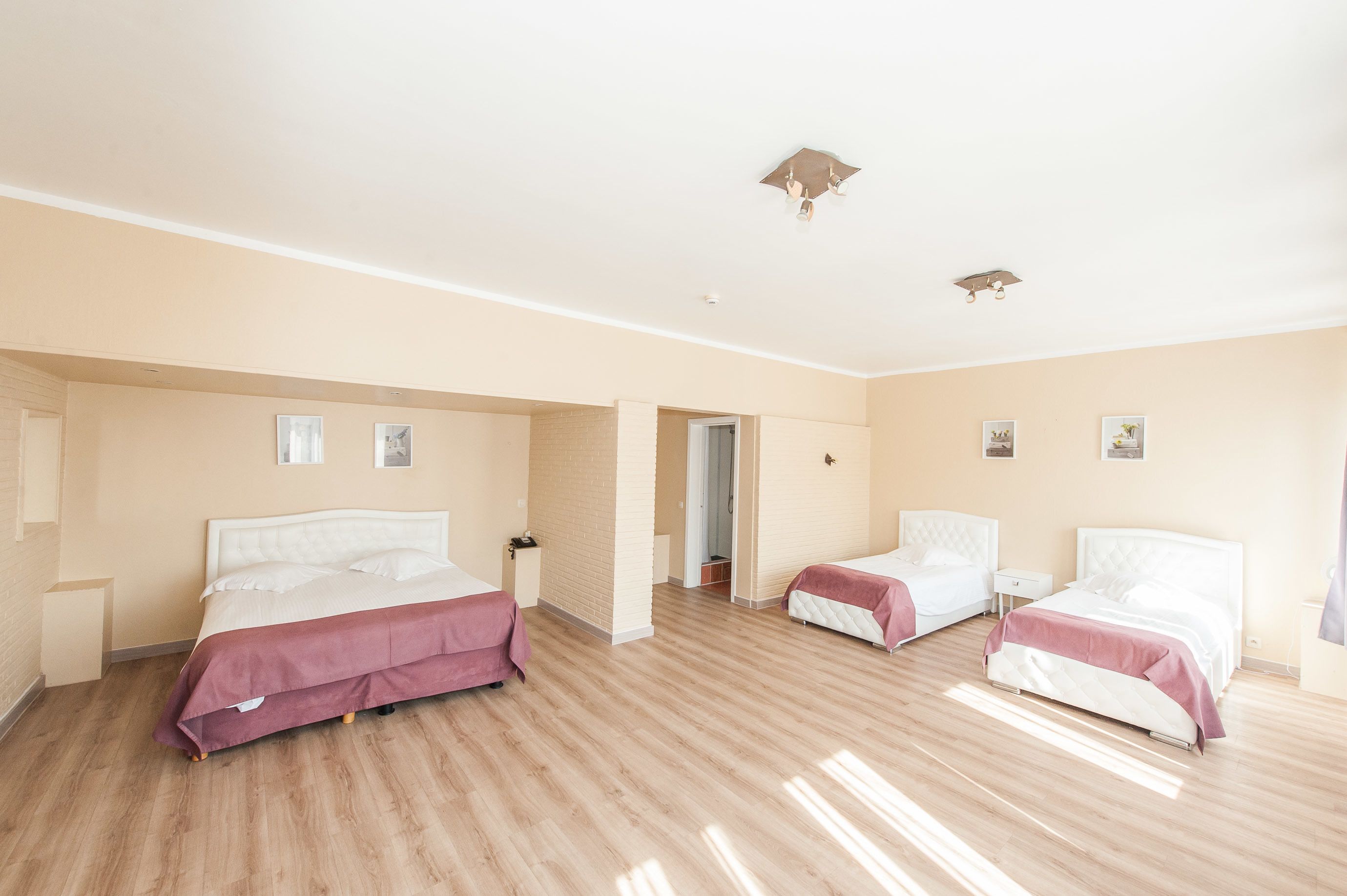 A hotel room with two beds, a wooden floor, and a beige wall.