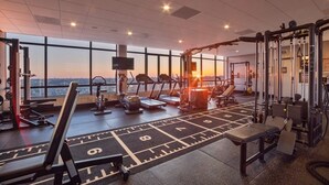 A gym with treadmills, weight machines, and a large window overlooking a cityscape.