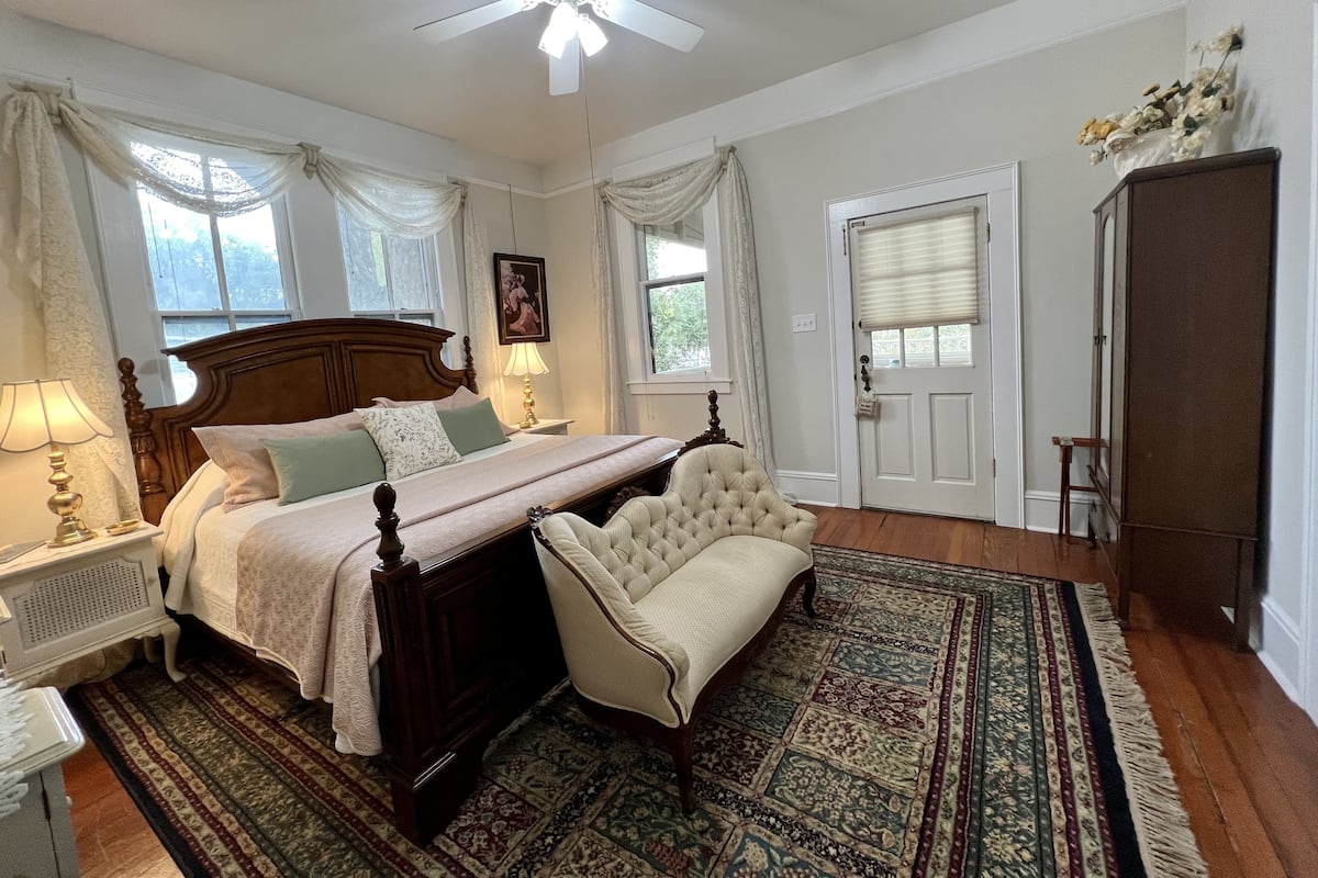 Une chambre avec un grand lit, une chaise, une armoire en bois et un ventilateur de plafond.
